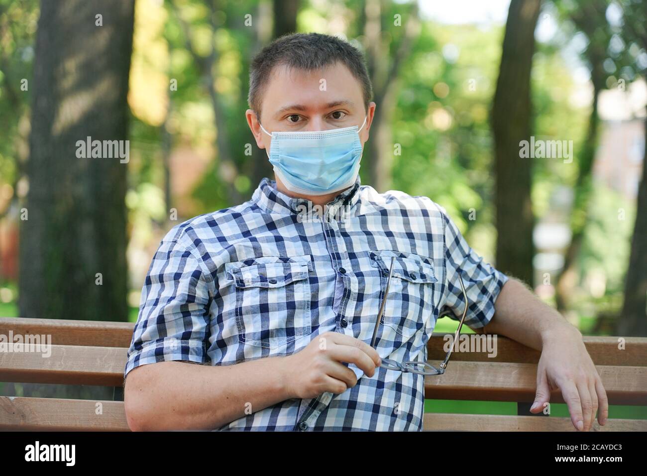 The guy in the mask from the virus sits on a park bench Stock Photo