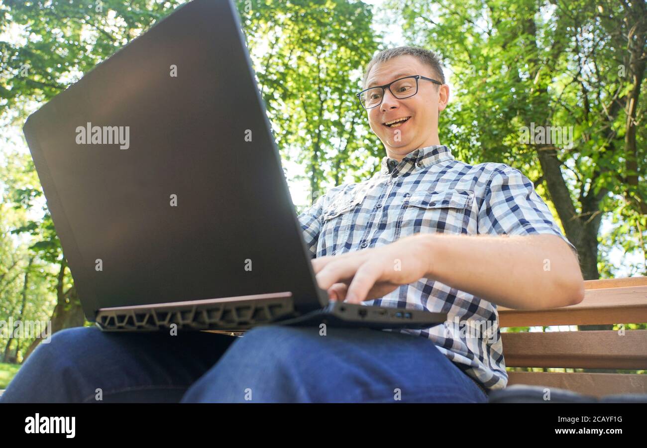 A guy with a laptop sits on a park bench. Stock Photo