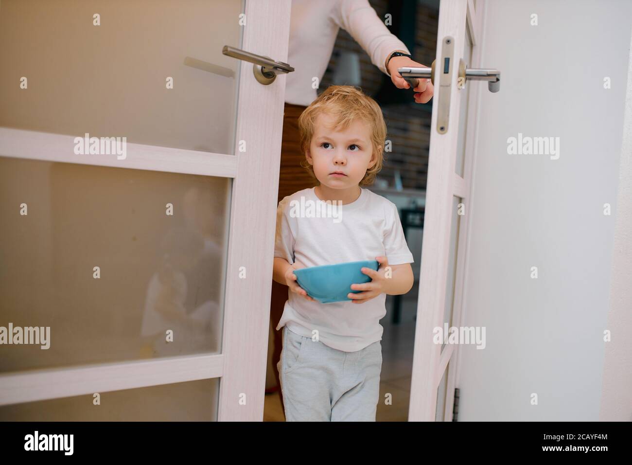 little caucasian boy, child stay near the door at home holding blue dish in hands, sweet child Stock Photo
