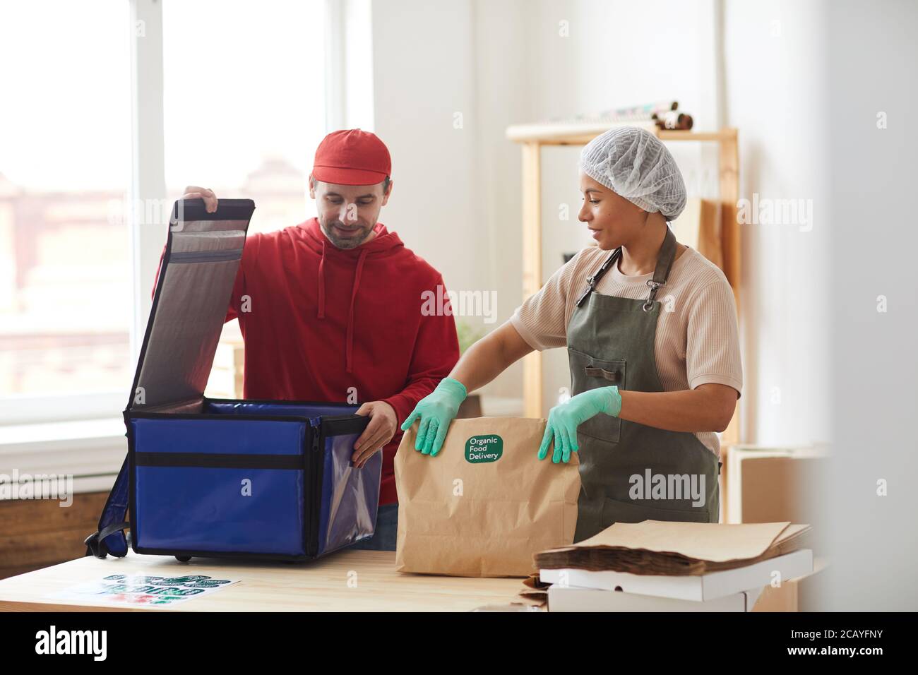 Waist up portrait of mature delivery man packing orders to cool box at food delivery service, copy space Stock Photo