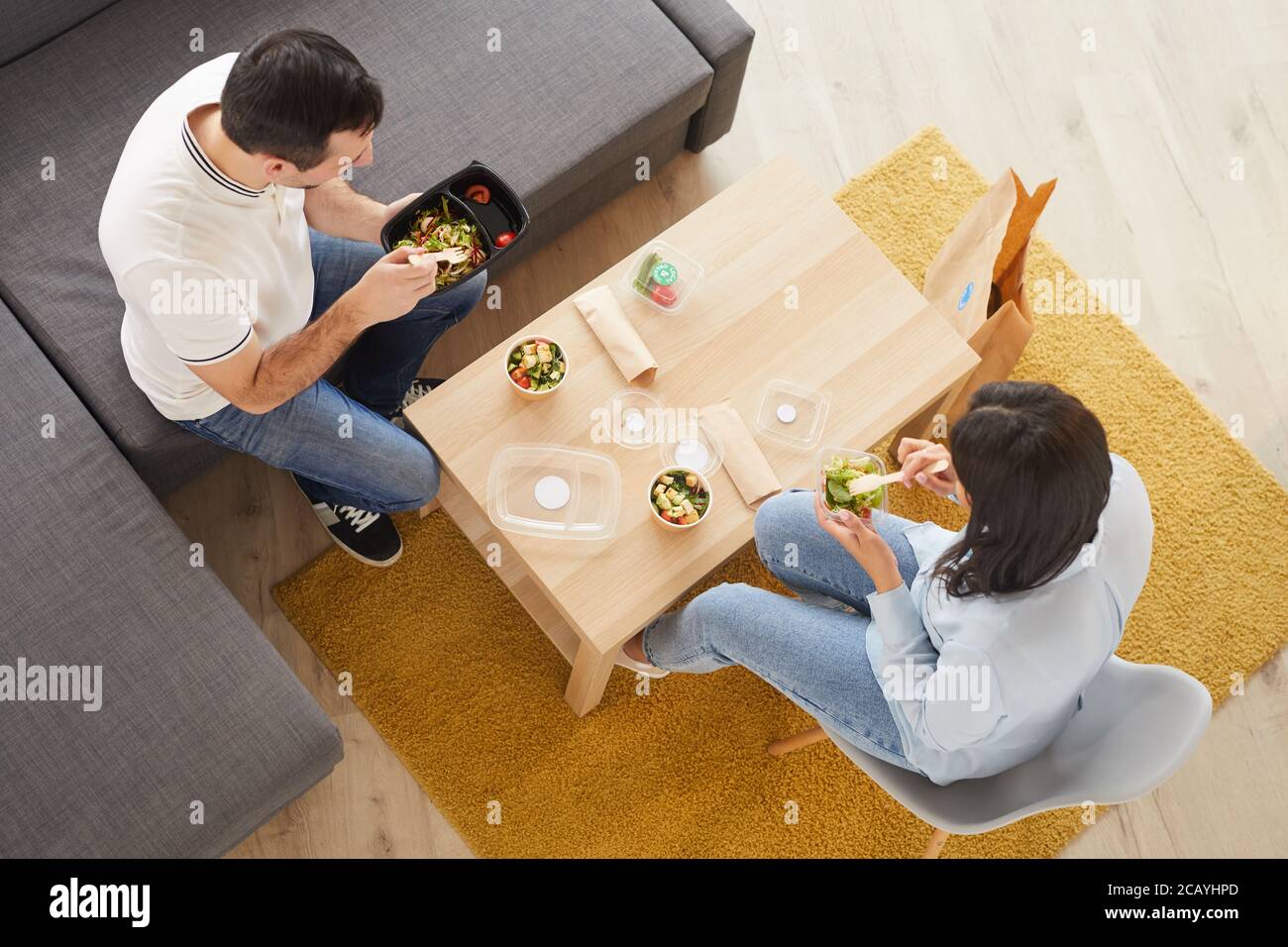 Above view portrait of man and woman eating takeout lunch in office or at home while sitting on big couch, copy space Stock Photo