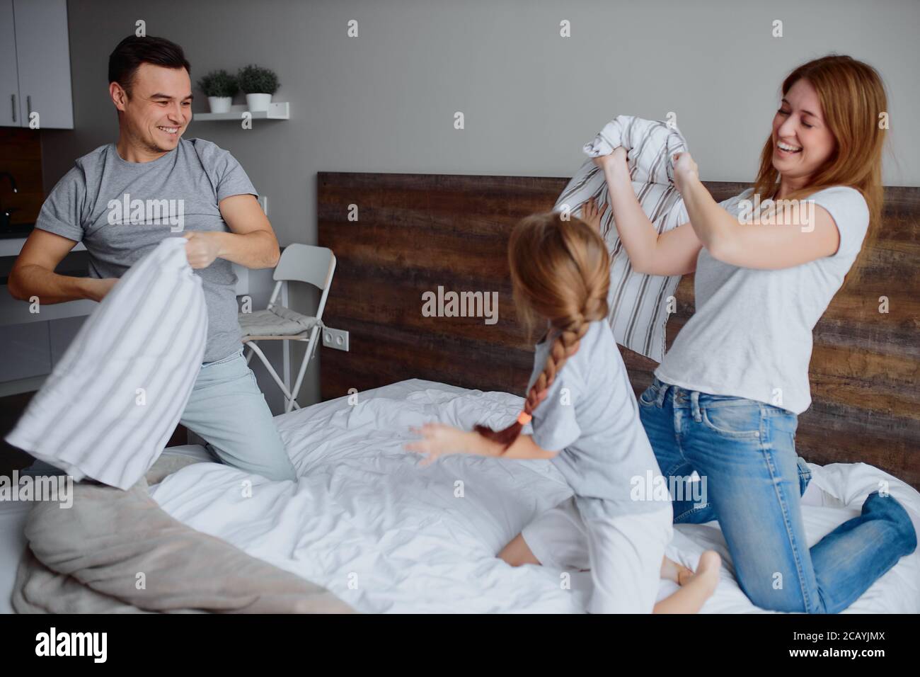beautiful happy and positive mother father and child girl play with each other with pillows, happy kid and parents Stock Photo