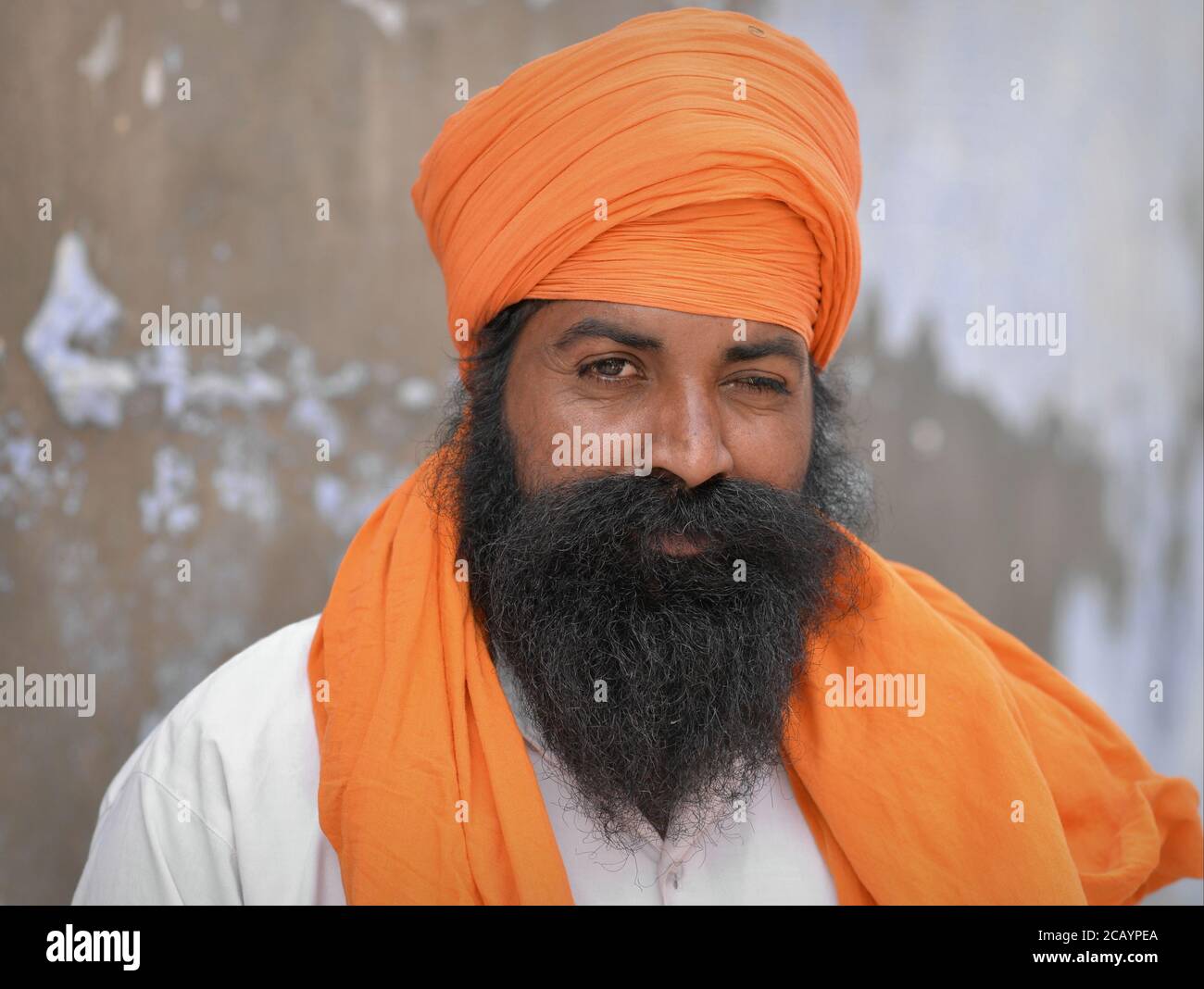Big middle-aged Indian Sikh man with orange turban (dastar) and orange shawl looks at the camera. Stock Photo