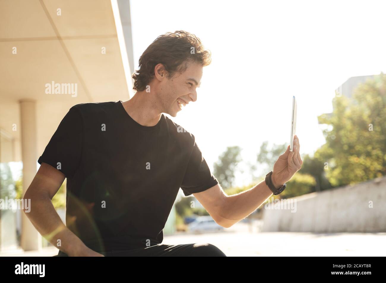 Cheerful young man using tablet for video chat at university campus on sunny day Stock Photo