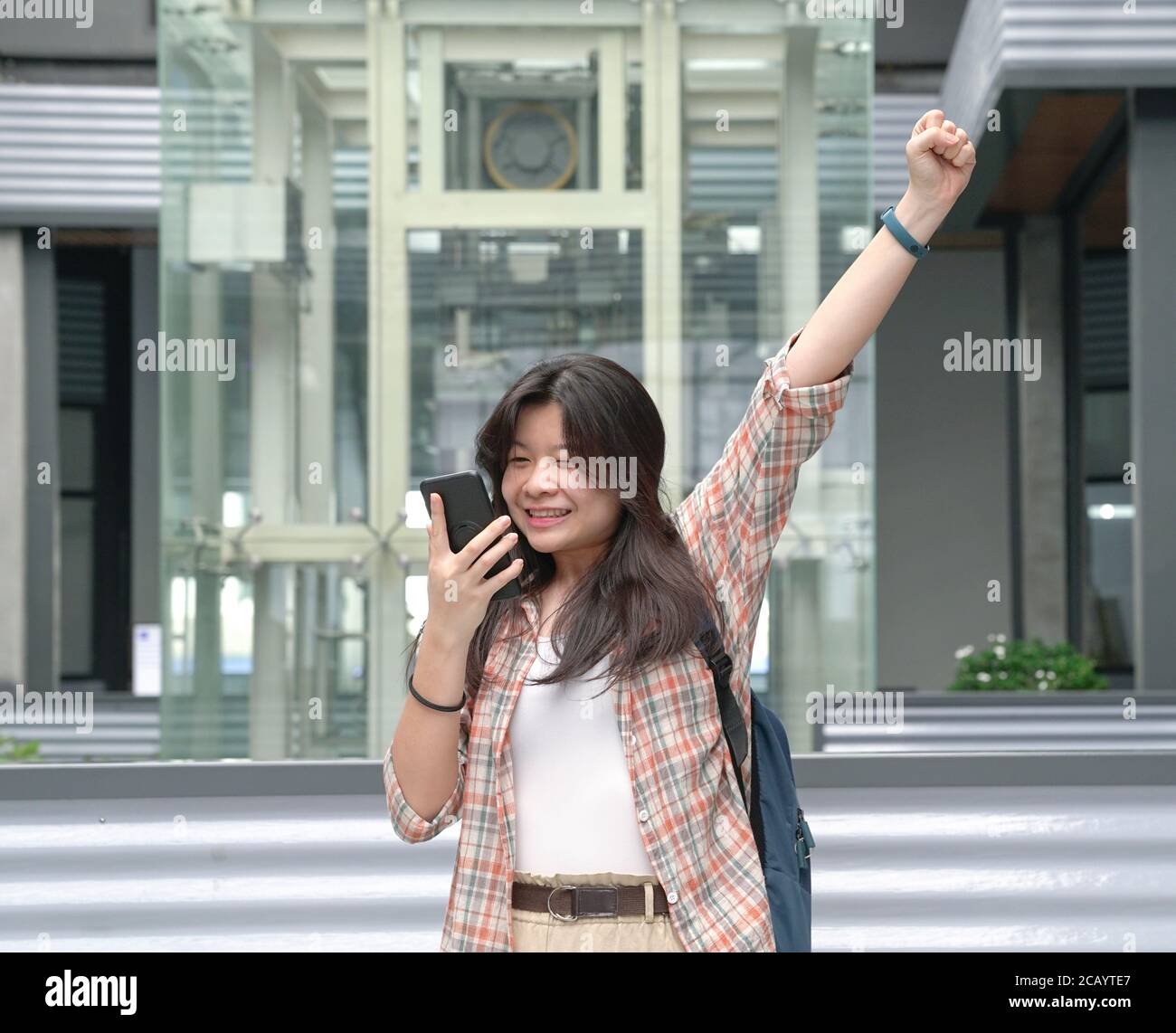 Asian woman react with joy by smiling happily and raising her hand while looking at her cellphone. Stock Photo
