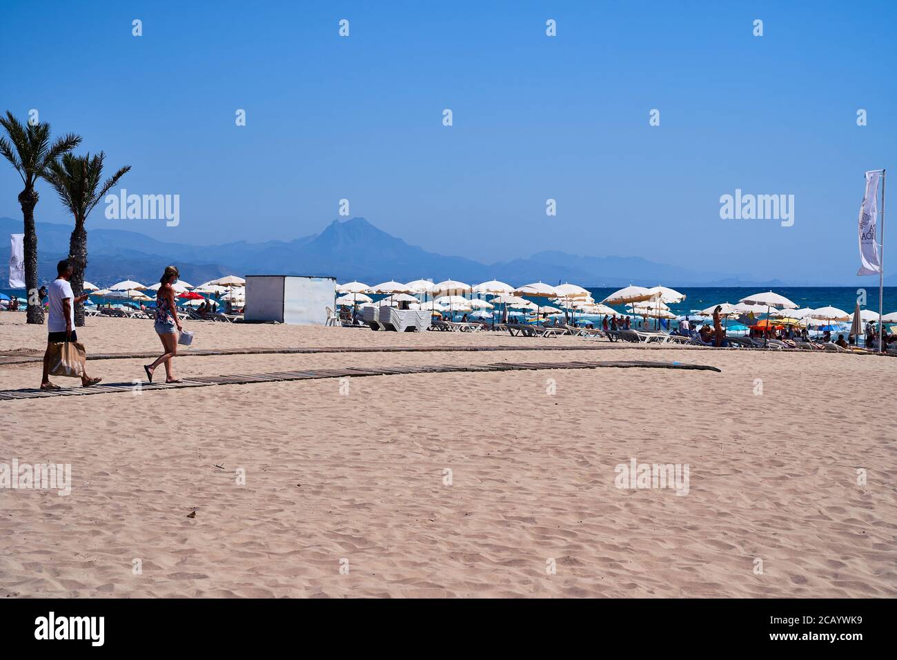 A couple wearing facemasks head onto the beach at Playa San Juan Alicante, Spain, Europe, July 2020 Stock Photo