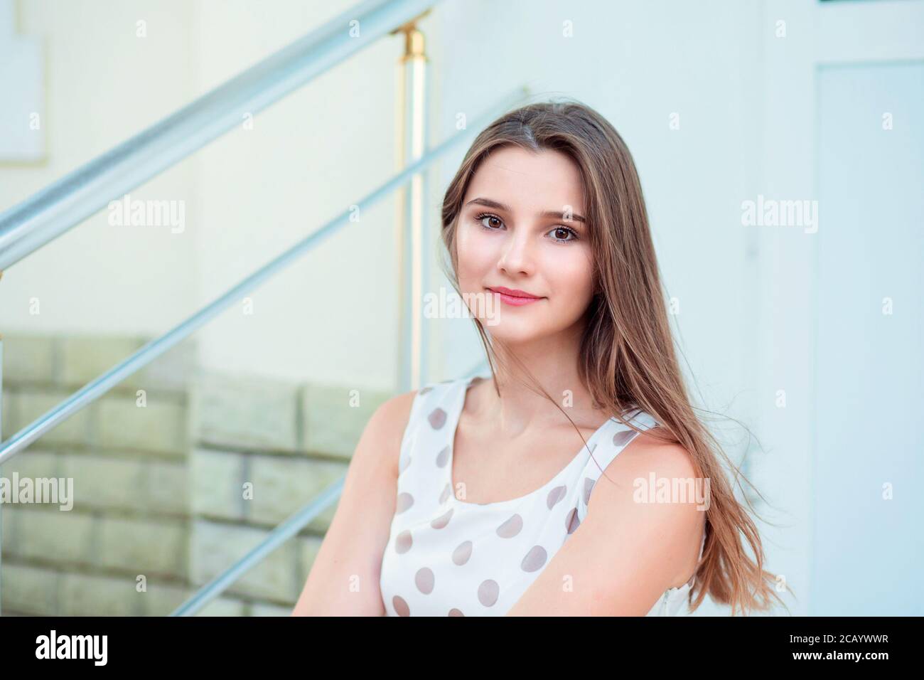 Teen girl with long brunette hair smiling sitting on steps Beautiful young girl in white dress  