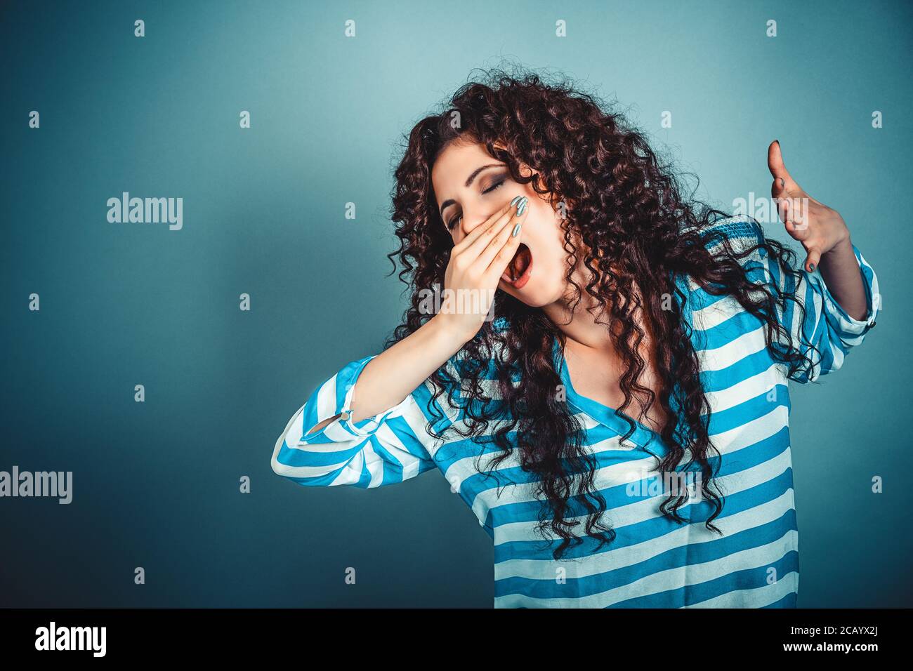 It is too early for me. Closeup portrait sleepy young woman with wide open mouth yawning eyes closed looking bored isolated blue wall background. Face Stock Photo