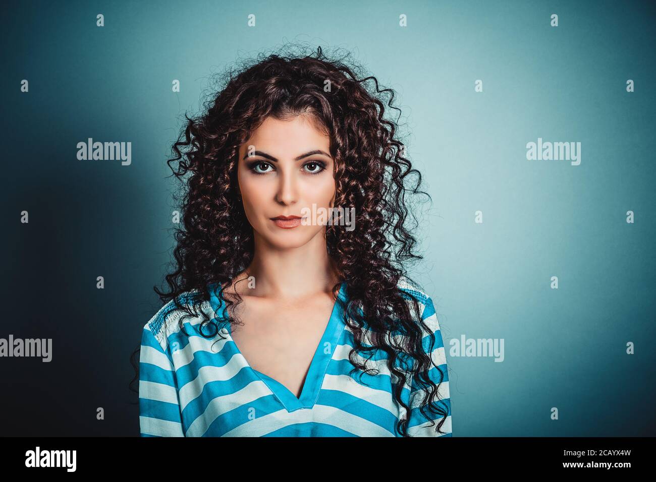 Success. Closeup portrait head shot confident beautiful young woman serious looking at you camera isolated blue background wall. Positive human emotio Stock Photo