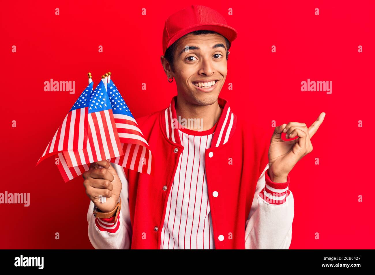 Young african amercian man wearing baseball uniform holding america flags smiling happy pointing with hand and finger to the side Stock Photo