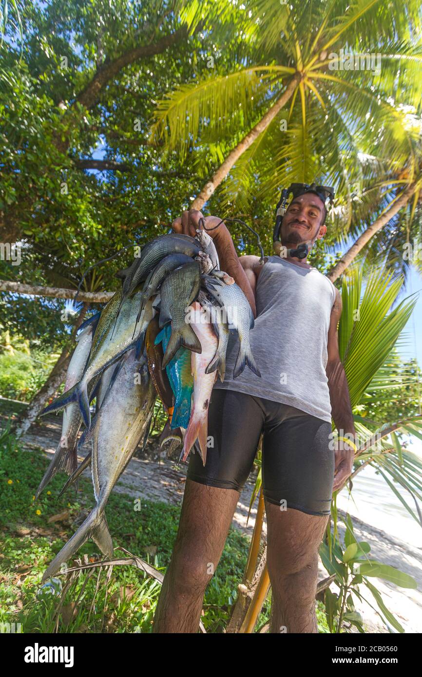 Man holds string of tropical fish he caught with a spear and snorkel gear. The fish include silver jacks, surgeon fish, gray emperors and more. Stock Photo
