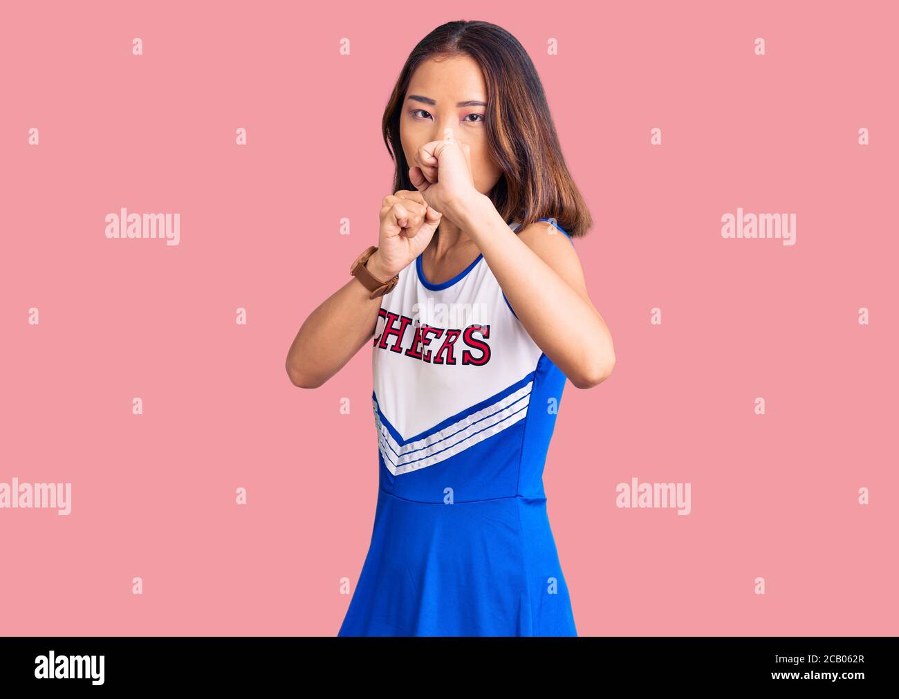 Young beautiful chinese girl wearing cheerleader uniform ready to fight with fist defense gesture, angry and upset face, afraid of problem Stock Photo