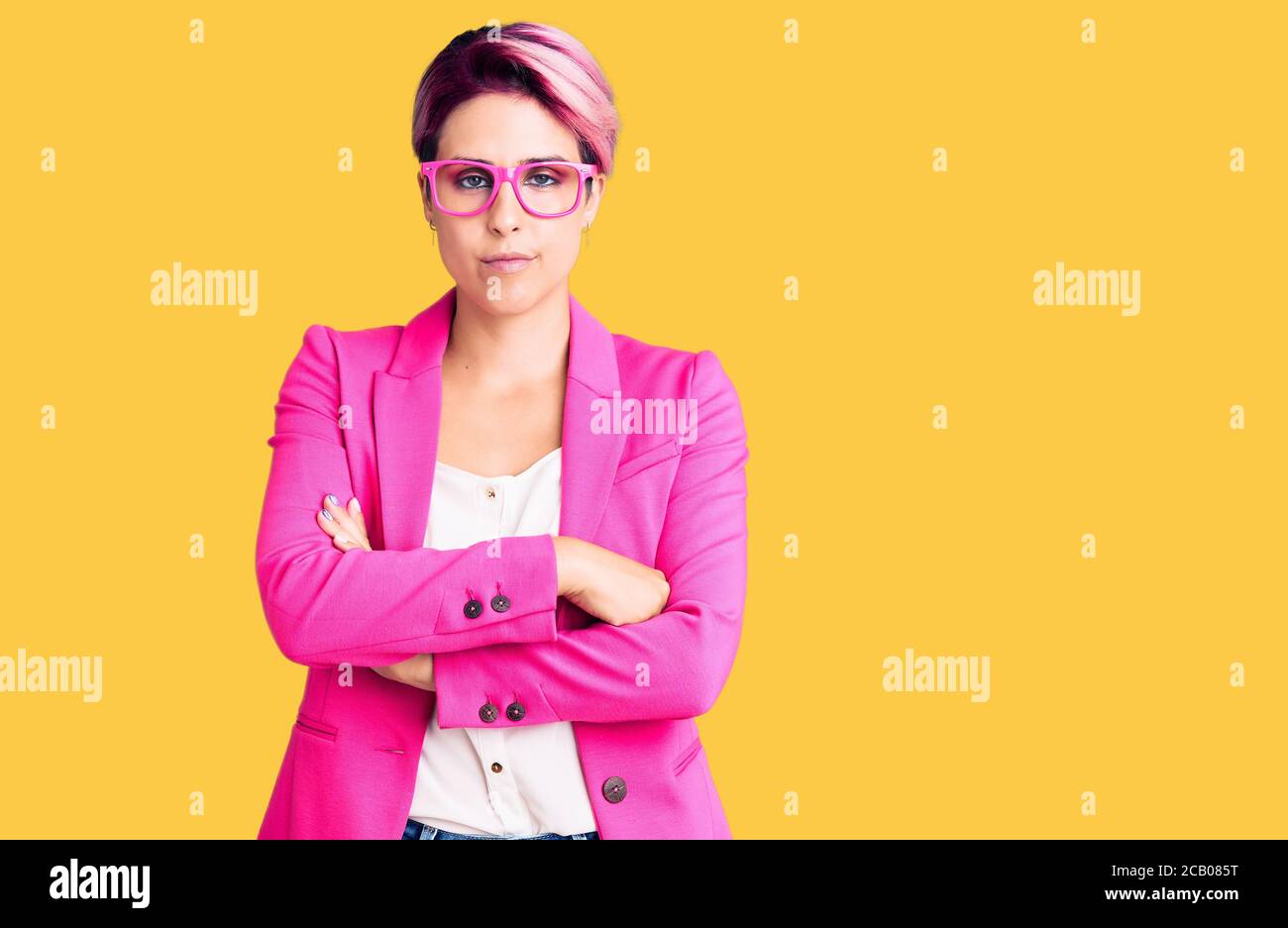 Young beautiful woman with pink hair wearing business jacket and glasses skeptic and nervous, disapproving expression on face with crossed arms. negat Stock Photo