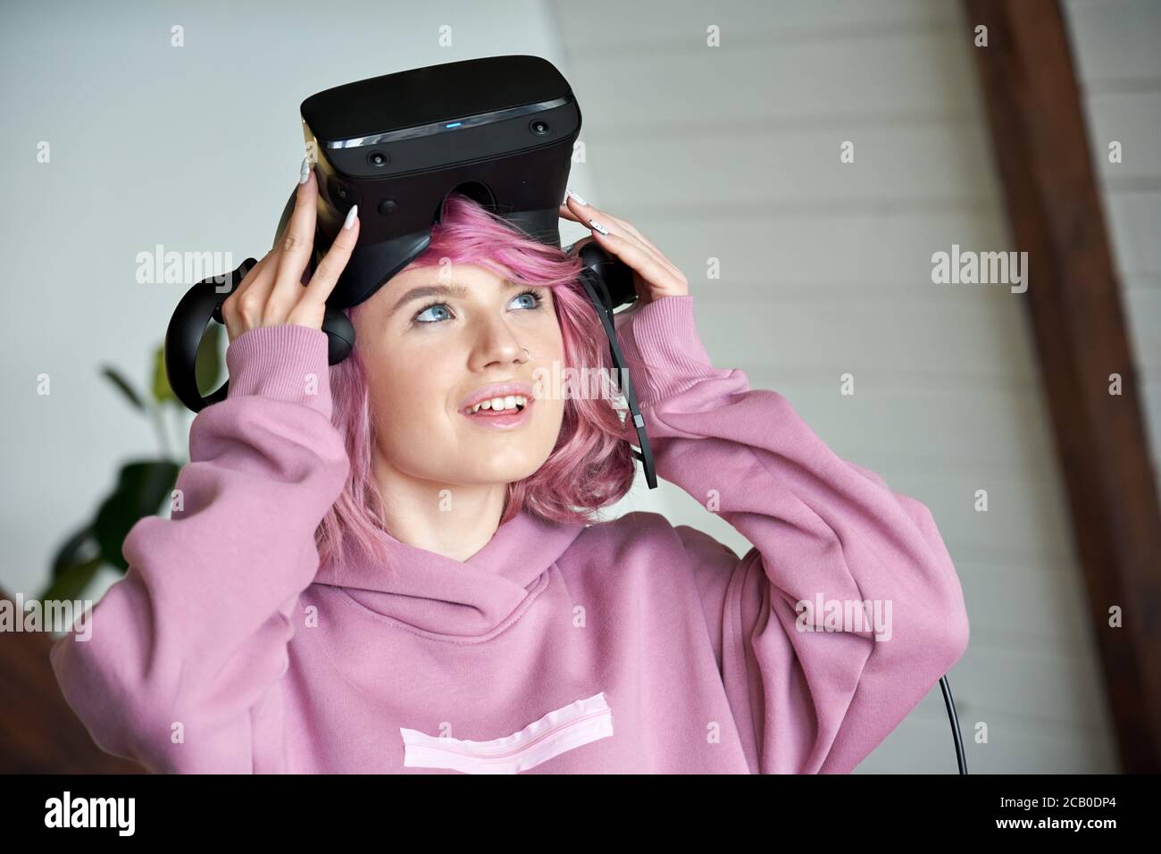 Excited teen girl with pink hair wear vr headset hold controller looking up. Stock Photo