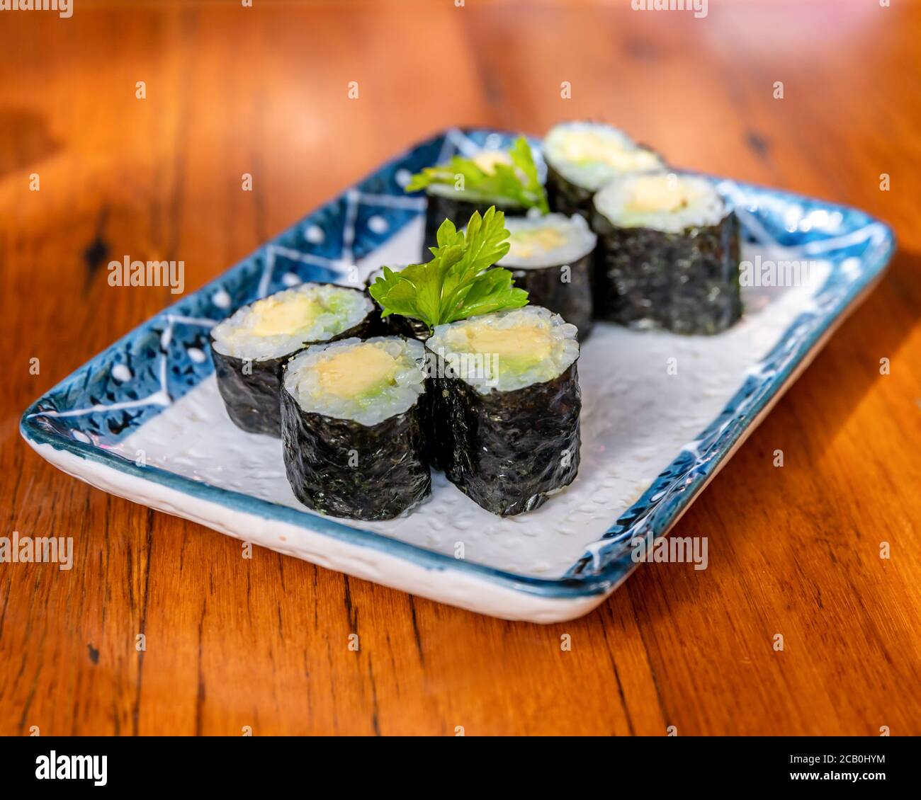 Mini Avocado Sushi Rolls on a rectangular plate and wooden table background blur Stock Photo
