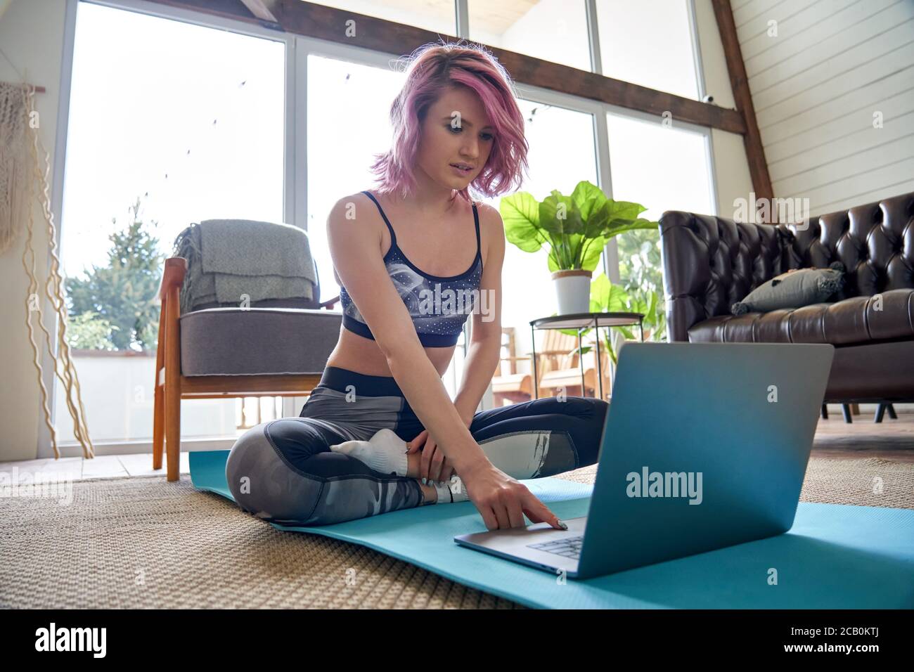 Young fit sporty hipster girl pink hair searching online fitness class at home. Stock Photo