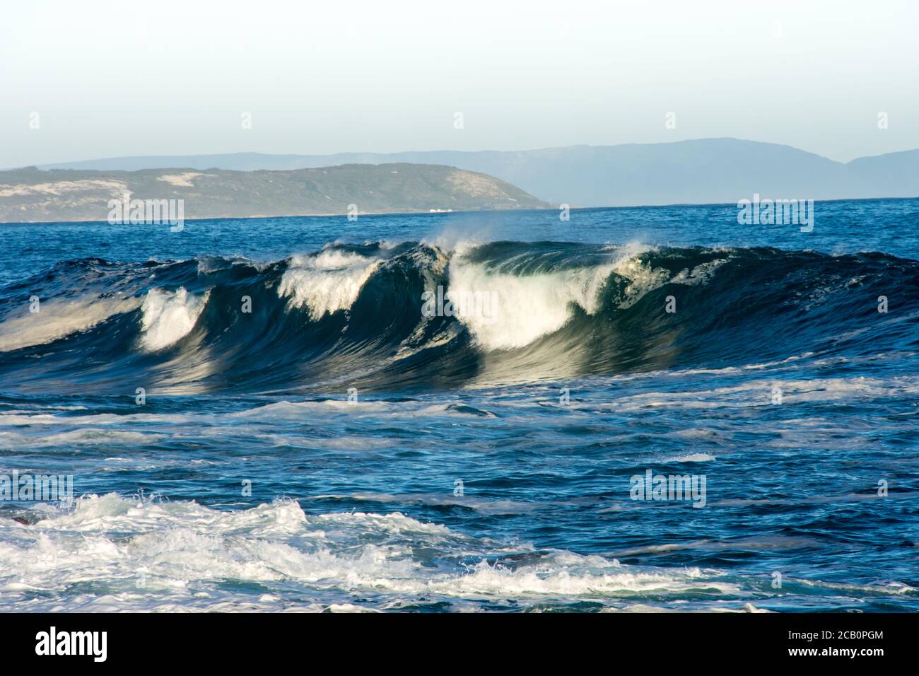 Wave breaking with sunlight reflecting from water and white foam blown in the wind seen from a side view Stock Photo