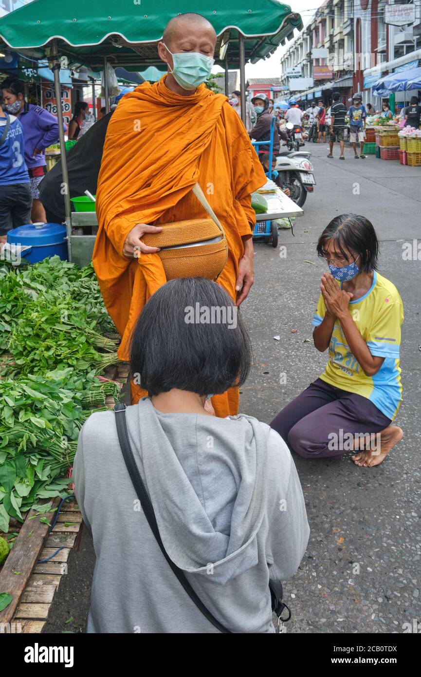 A Buddhist monk during his traditional morning alms round (binta baat) blessing two female kneeling and praying worshippers;  Phuket Town, Thailand Stock Photo