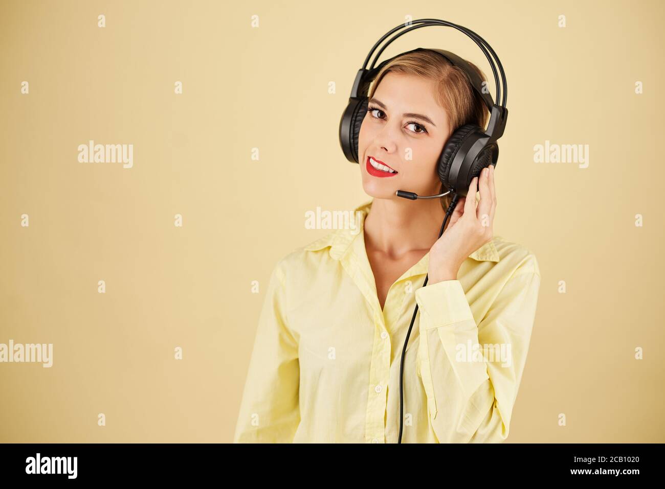 Portrait of technical support operator in headset having problems with connection, isolated on light yellow Stock Photo