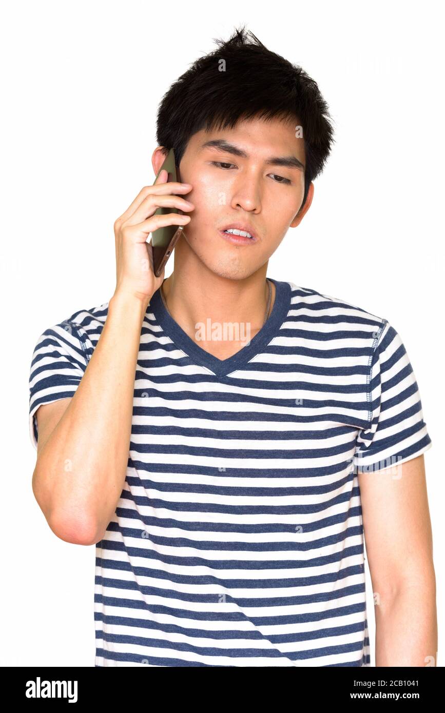 Studio shot of young handsome Asian man talking on mobile phone isolated against white background Stock Photo
