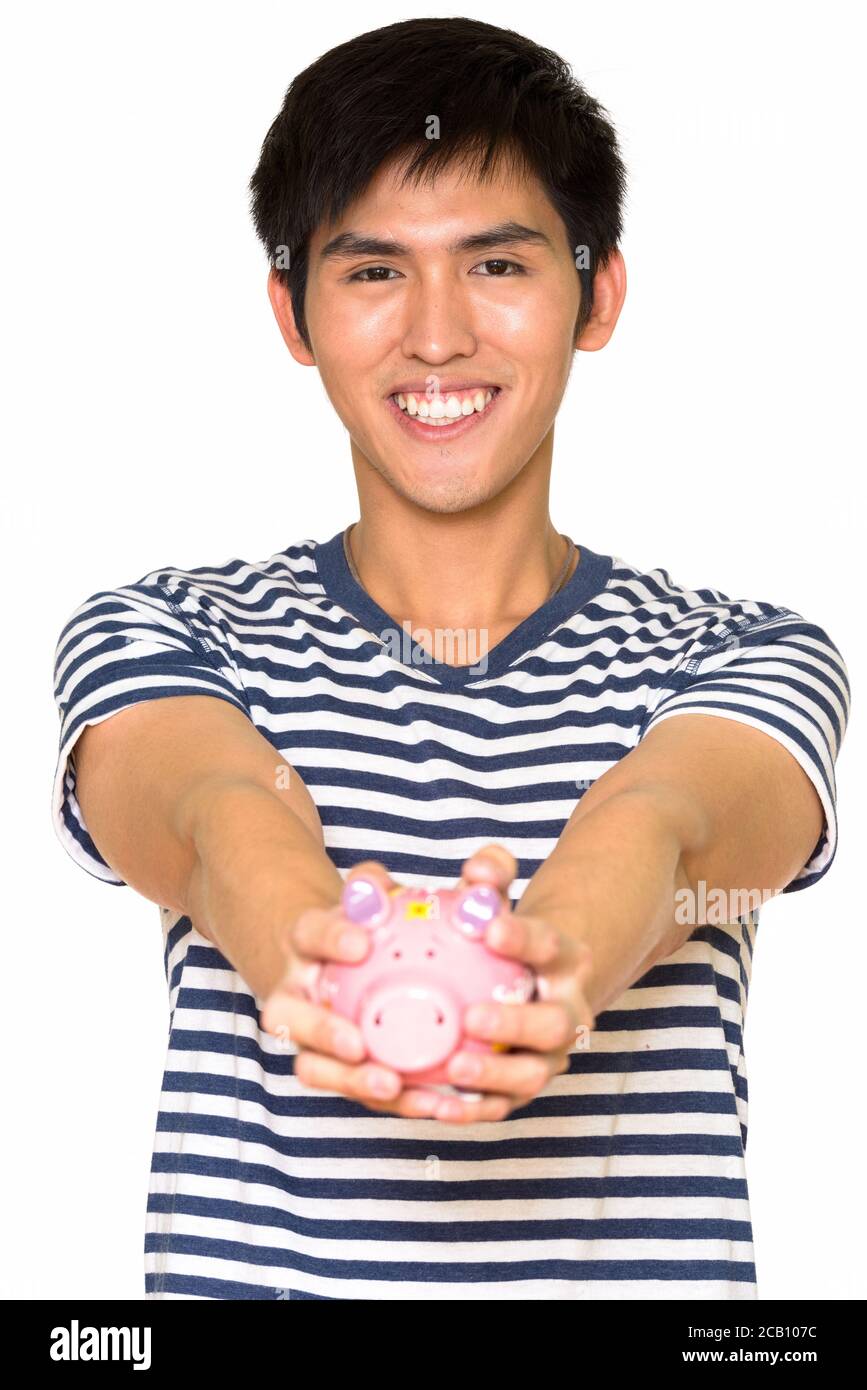Studio shot of young handsome Asian man holding piggy bank isolated ...