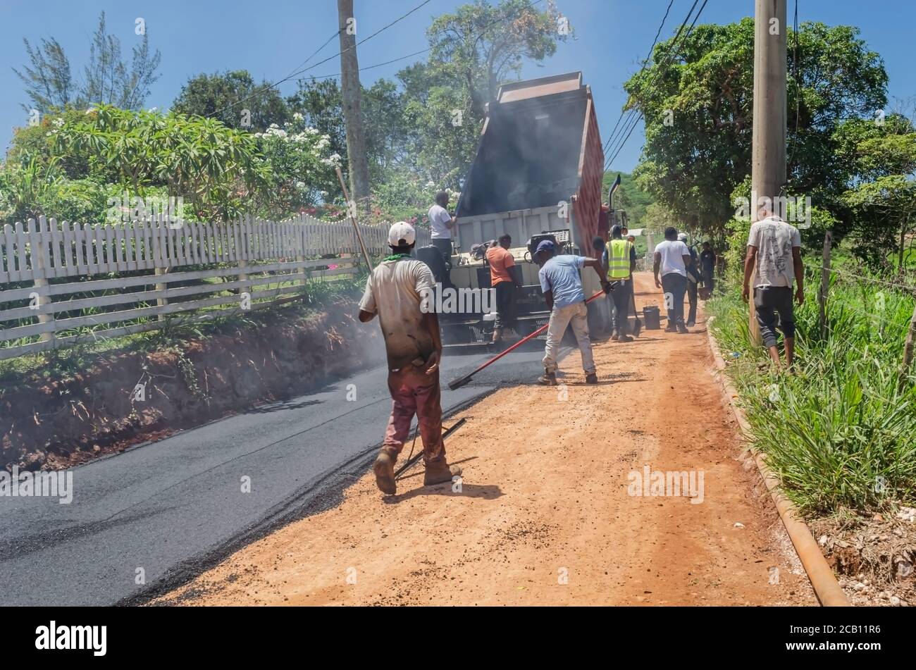Road repairs in progress from Mayfield to Lovers Leap, Jamaica, as men spread asphalt concrete from a truck with paver and other tools. Stock Photo