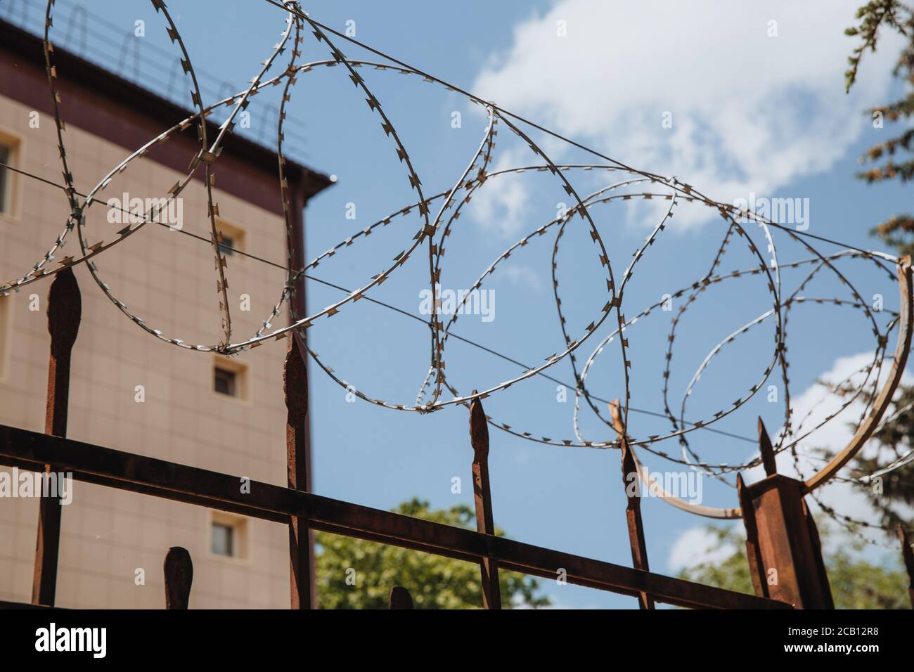 Building wall behind barbed wire barrier with beautiful heavenly clouds. Stock Photo