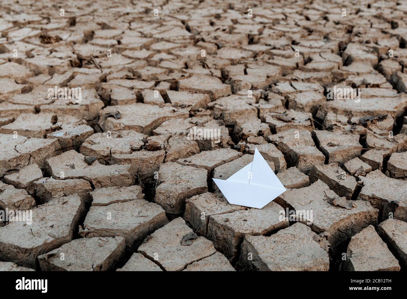 White paper boat on dry, dry soil with cracks. Global warming concept. Stock Photo