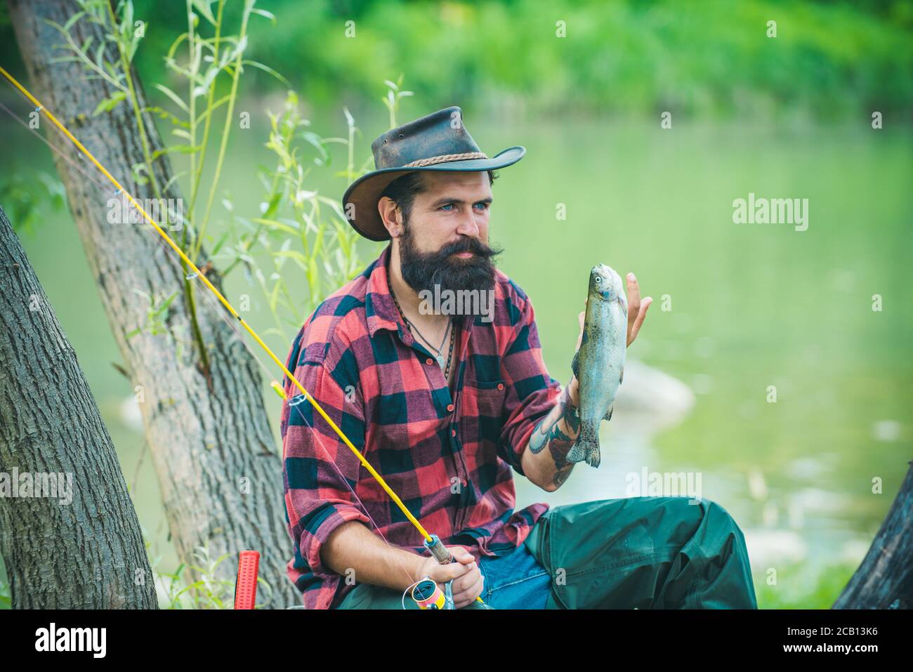 Man relaxing and fishing by lakeside. Hobby sport activity. Man fishing on the lake. Portrait of cheerful bearded man fishing. It is so big. Fishing Stock Photo