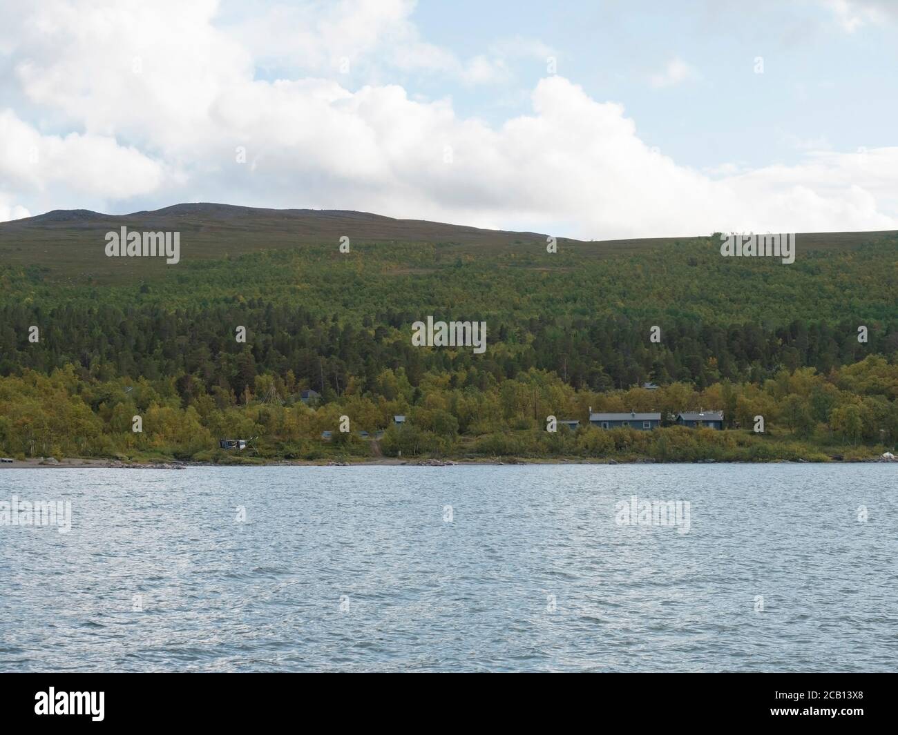 view on sami hut in Saltoluokta from river Lulealven with green mountains, birch tree and blue sky white clouds Stock Photo