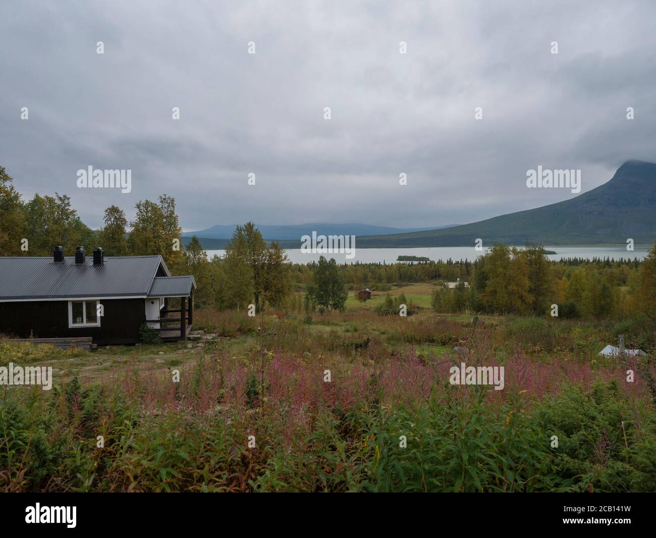 View on Aktse Fjallstuga STF mountain cabin hut at Sweden Lapland with Laitaure lake, green hills and birch tree. Cloudy rainy day on the Kungsleden Stock Photo