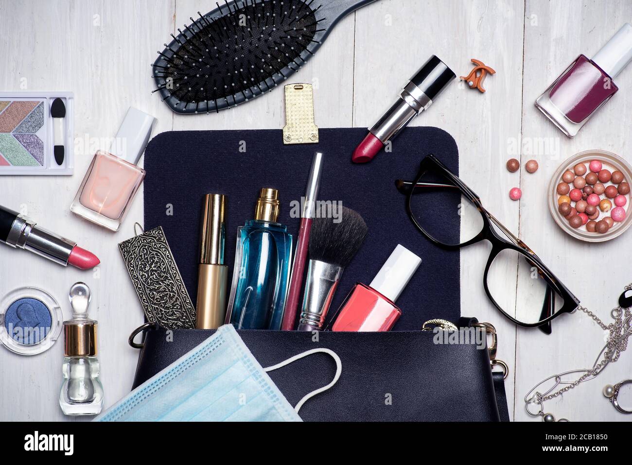 Surgical face mask with various makeup and cosmetic products falling out of an female bag tabletop flat lay Stock Photo