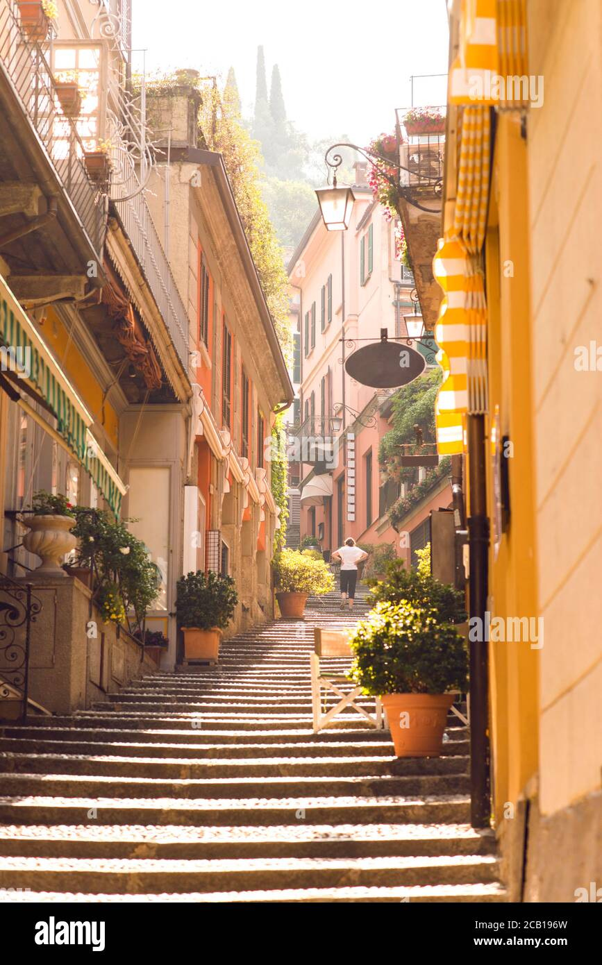 Sunrise on Old Picturesque Street in Bellagio City. Lombardy. Italy. Early Morning without Tourists. Woman Go Up on Staircase. Stock Photo