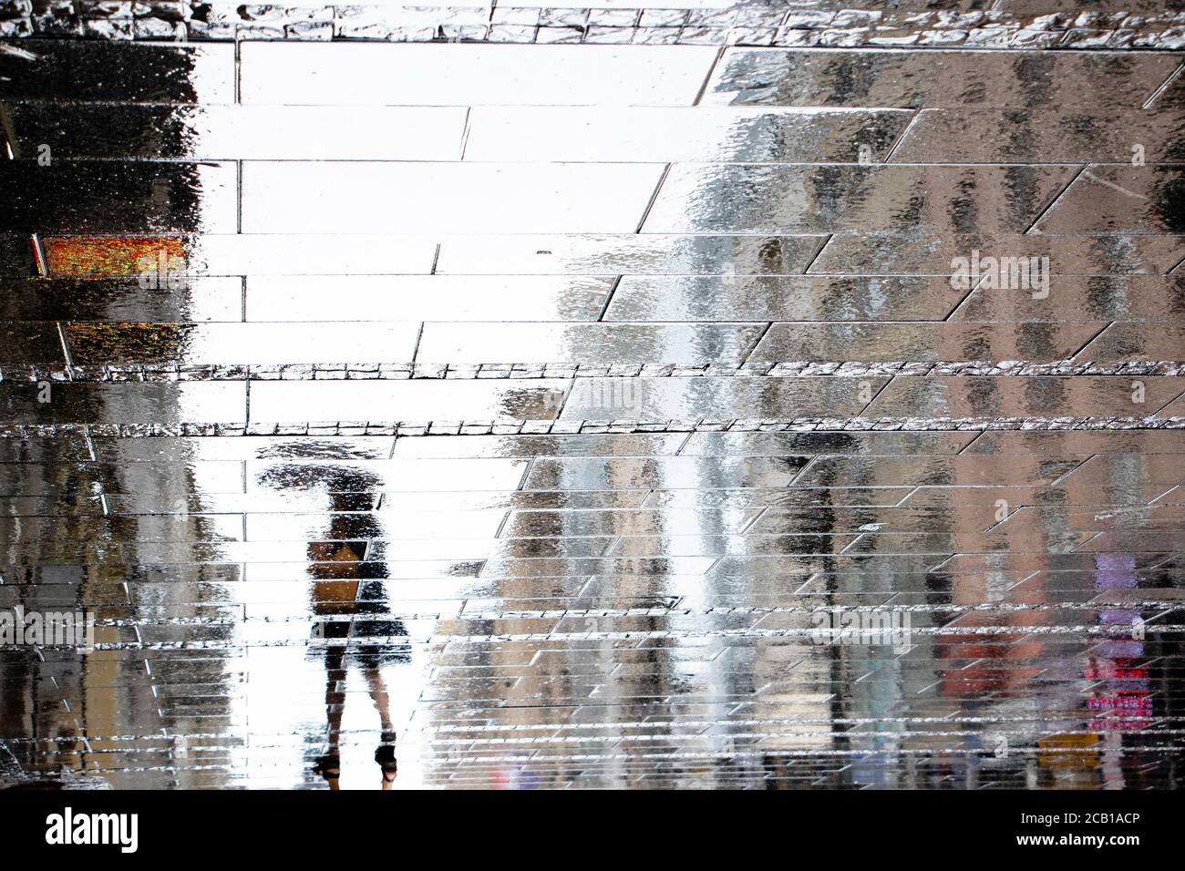 Blurry reflection shadow silhouette on wet puddle of a woman under umbrella walking a city street on a rainy day, abstract background Stock Photo