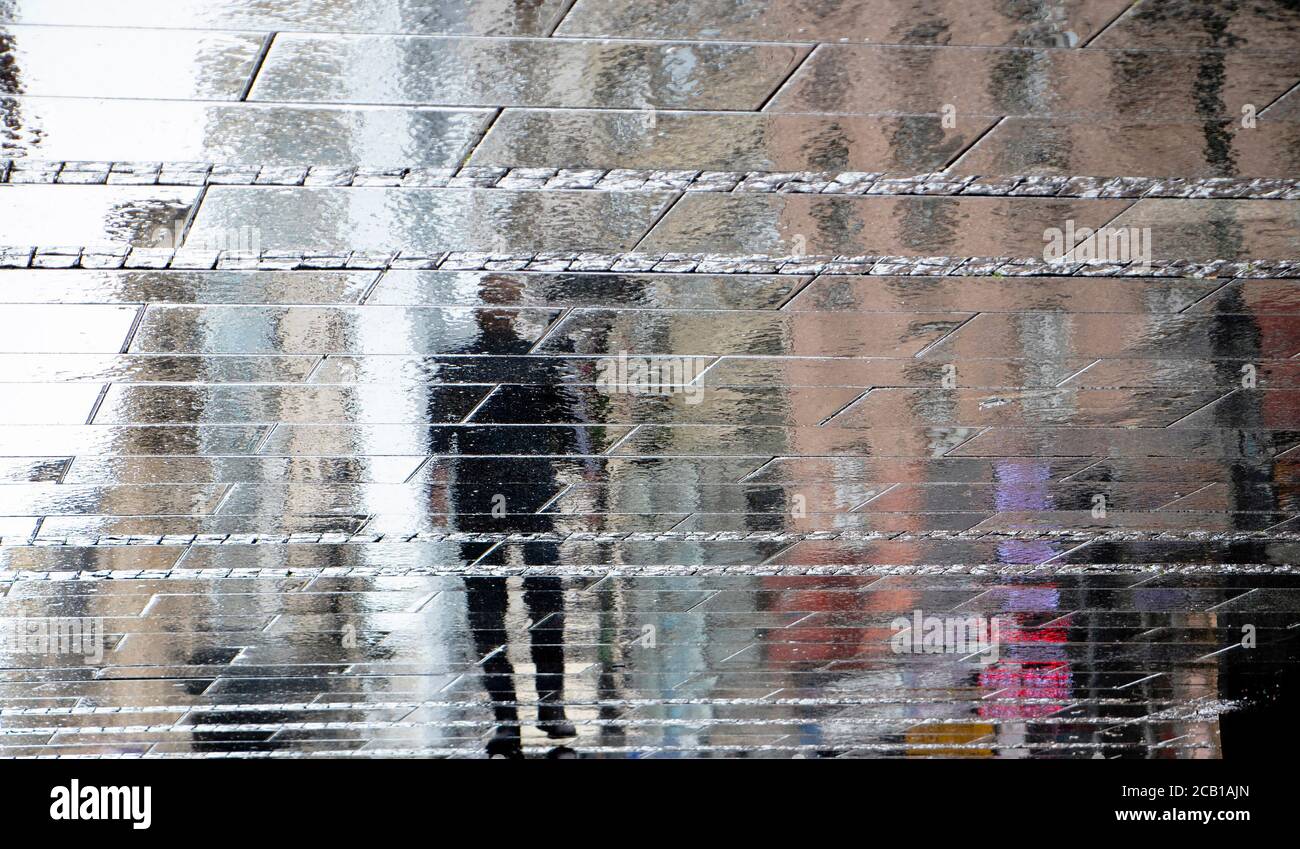 Blurry reflection shadow silhouette on wet puddle of a man walking a city street on a rainy day, abstract background Stock Photo