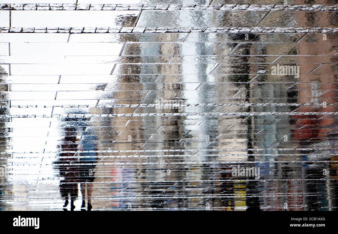Blurry reflection shadow silhouette on wet puddle of a couple walking a city street on a rainy day, abstract background Stock Photo