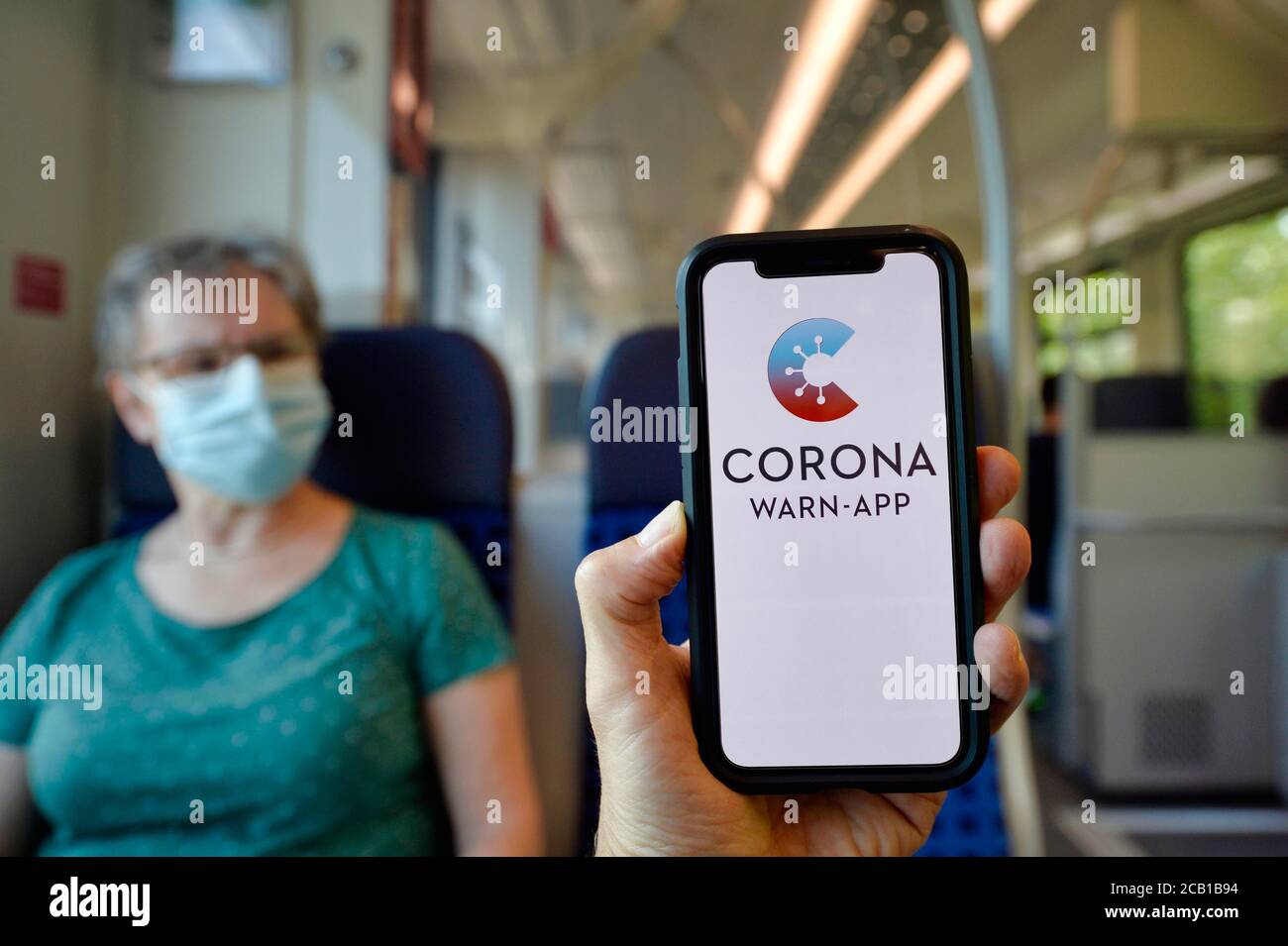 Hand holds smartphone with corona warning app in front of elderly woman with face mask sitting in S-Bahn, train, corona crisis, Stuttgart Stock Photo