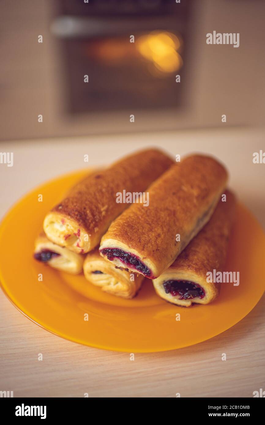 Buns with black currant jam in orange plate on the kitchen table. Background turned oven Stock Photo