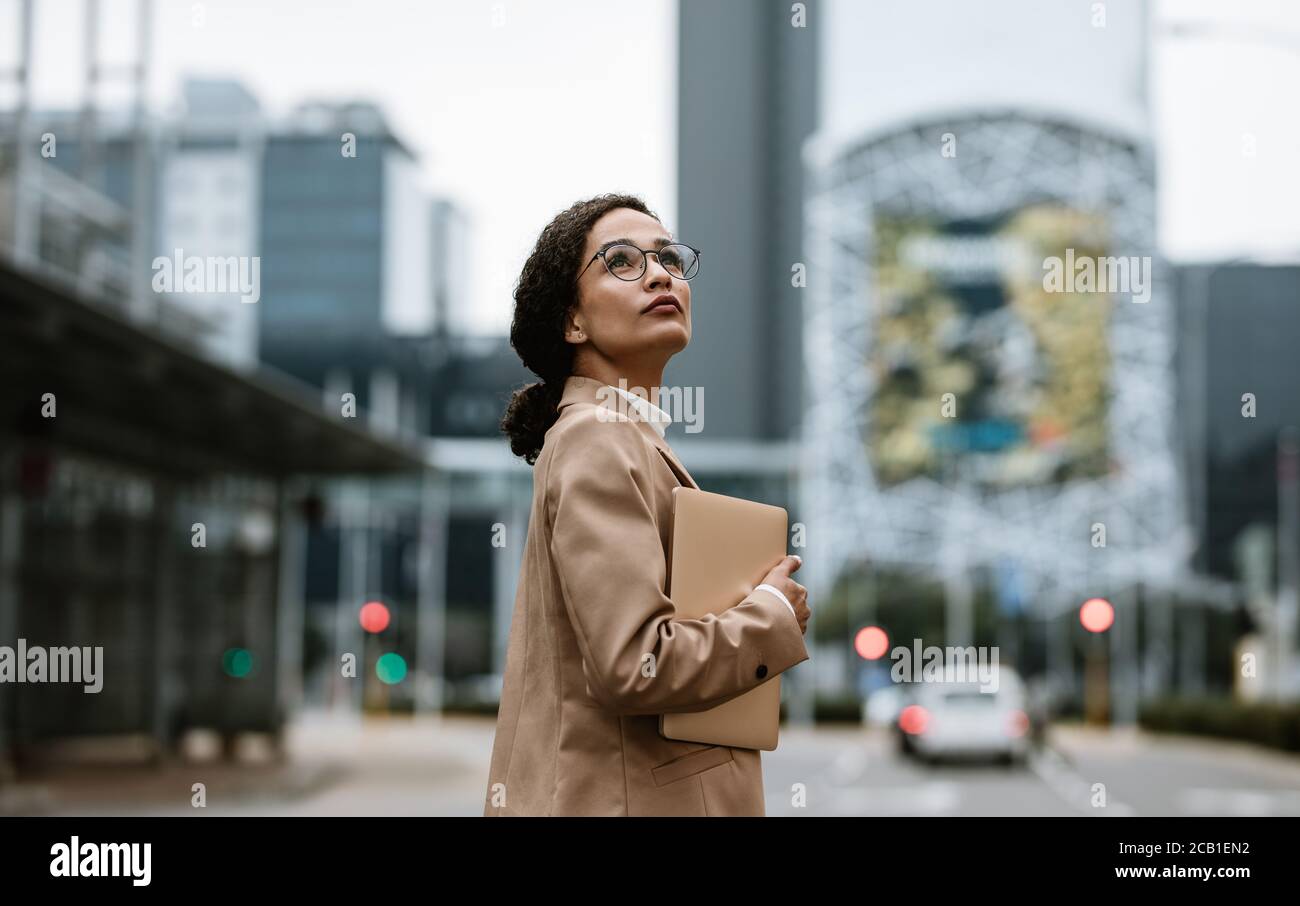 Businesswoman with a digital tablet looking up over her shoulder. Female business professional looking back at her office building. Stock Photo