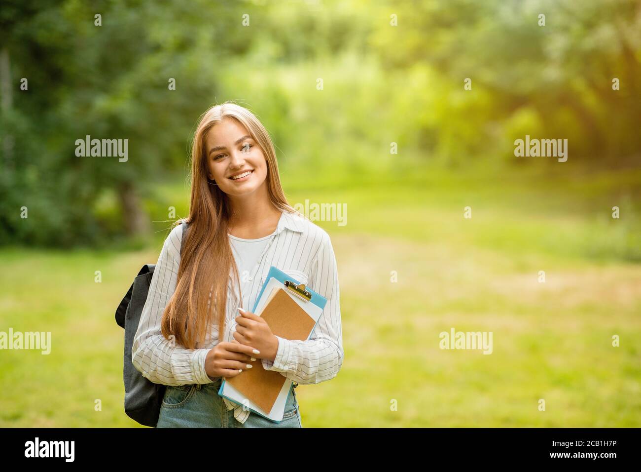 Outdoor Portrait Of Smiling College Student Girl With Backpack And Workbooks Stock Photo