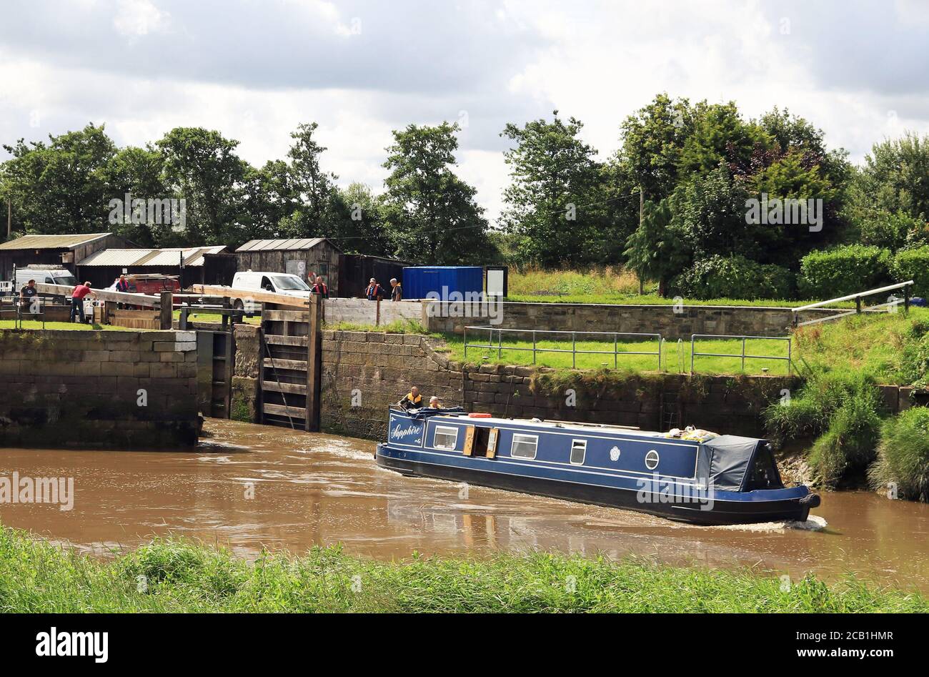 A blue canal narrow boat “Sapphire” leaving Tarleton Sea lock pushes against the incoming tide as it sets out to cross the Ribble Link. Stock Photo