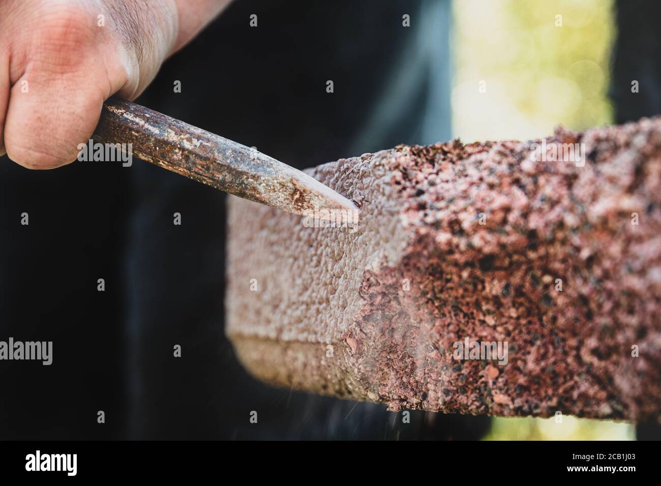 Close-up of a man cutting stone with a chisel, craftsman tears down a wall Stock Photo