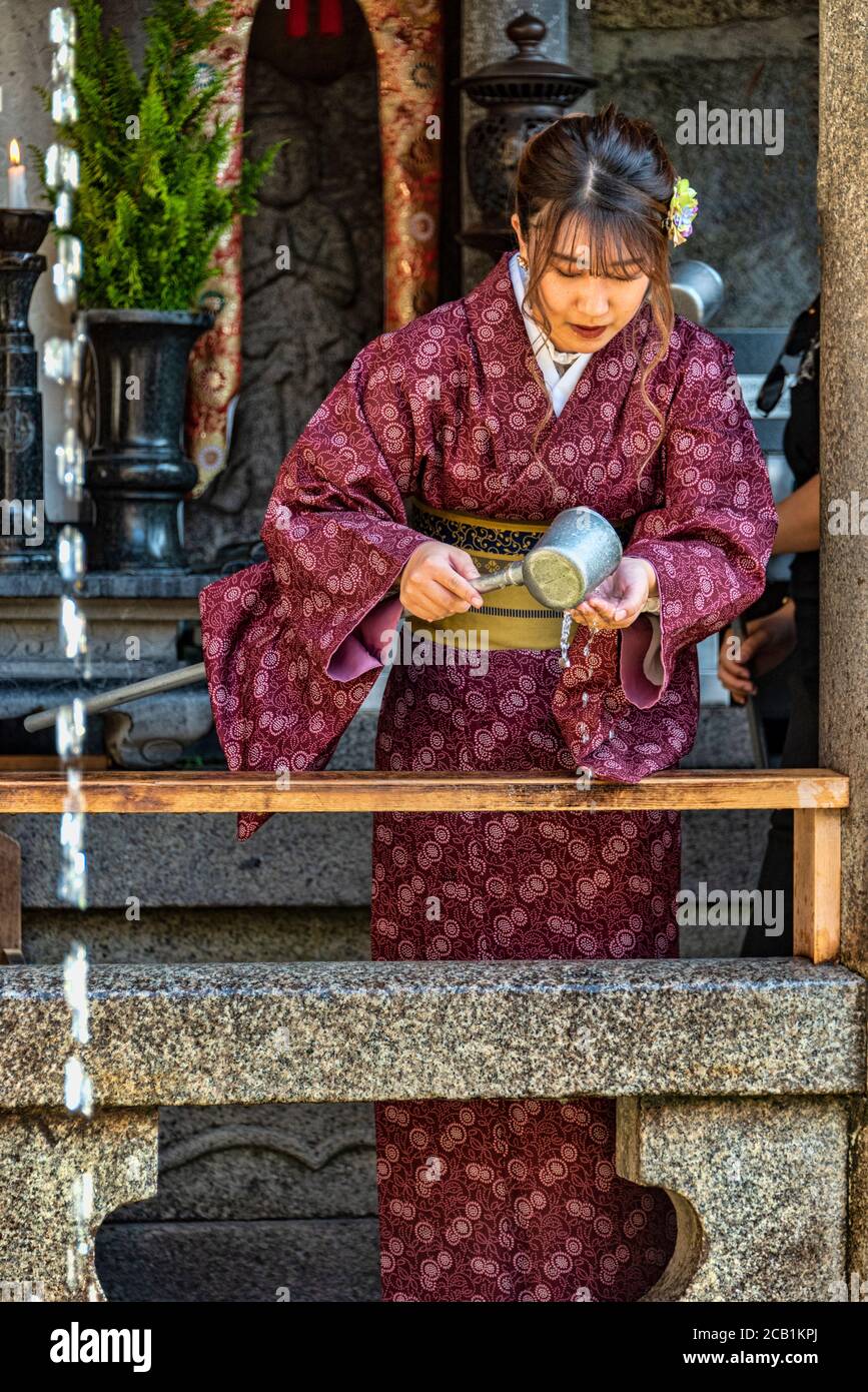 Young woman in kimono garment drinking from the OtowanoTaki waterfall