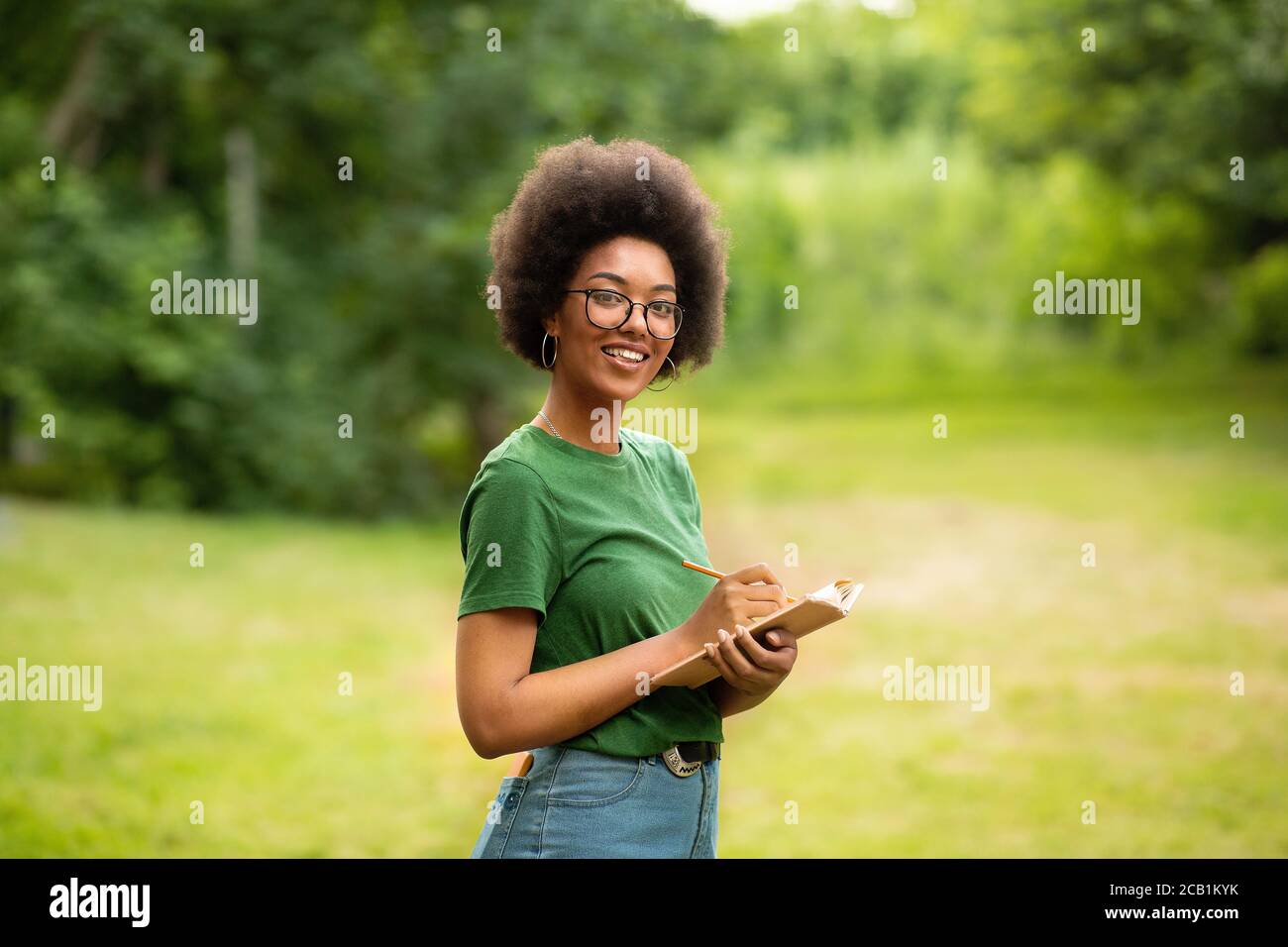 Portrait Of Cheerful Black Student Girl With Book In Hands Posing Outdoors Stock Photo