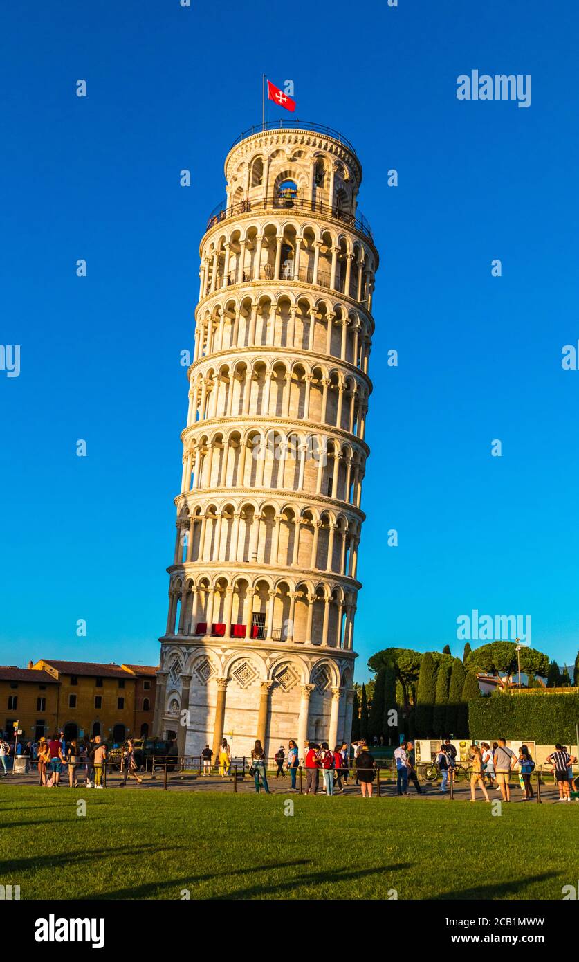 A picturesque portrait shot of the famous Pisa Leaning Tower on a beautiful day at dusk with a blue sky, and the sun shines on the white marbled... Stock Photo