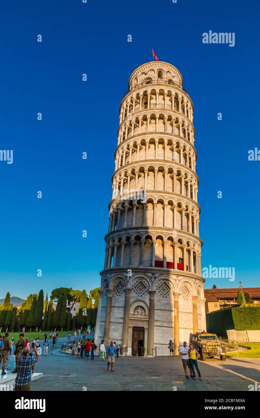 Nice portrait shot of the famous Pisa Leaning Tower with entrance door on a beautiful day at dusk with a blue sky, and the sun shines on the white... Stock Photo