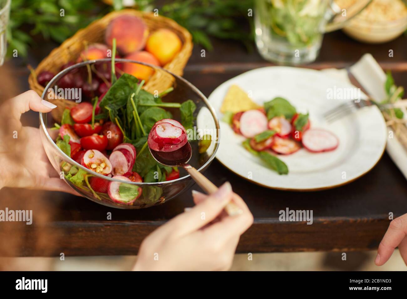 Close up of unrecognizable woman holding fresh vegetable salad while enjoying dinner with friends and family outdoors, copy space Stock Photo