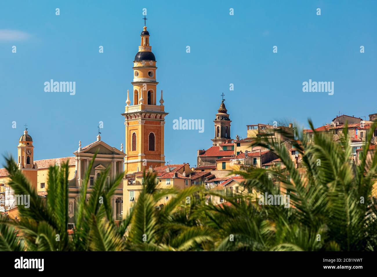 Bell tower of Basilica of Saint Michel Archange under blue sky as seen through the palms in old town of Menton, France. Stock Photo