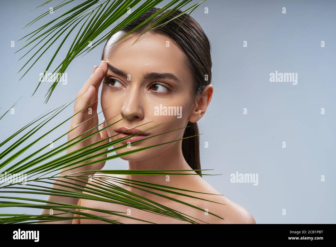 Charming young woman standing behind green plant Stock Photo