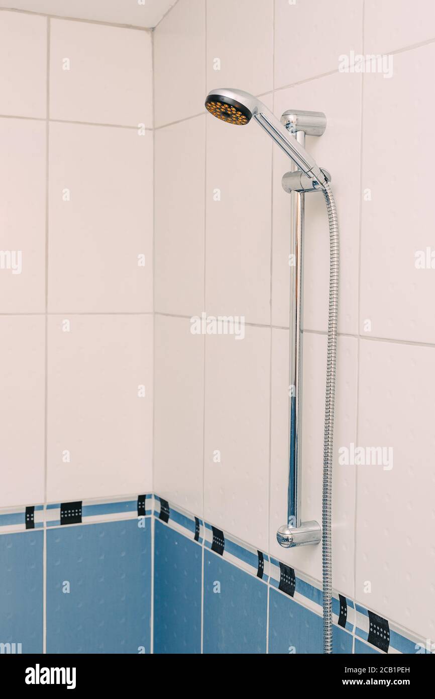 https://c8.alamy.com/comp/2CB1PEH/hand-shower-with-long-hose-in-a-wall-holder-in-a-bathroom-with-white-and-blue-tiles-2CB1PEH.jpg